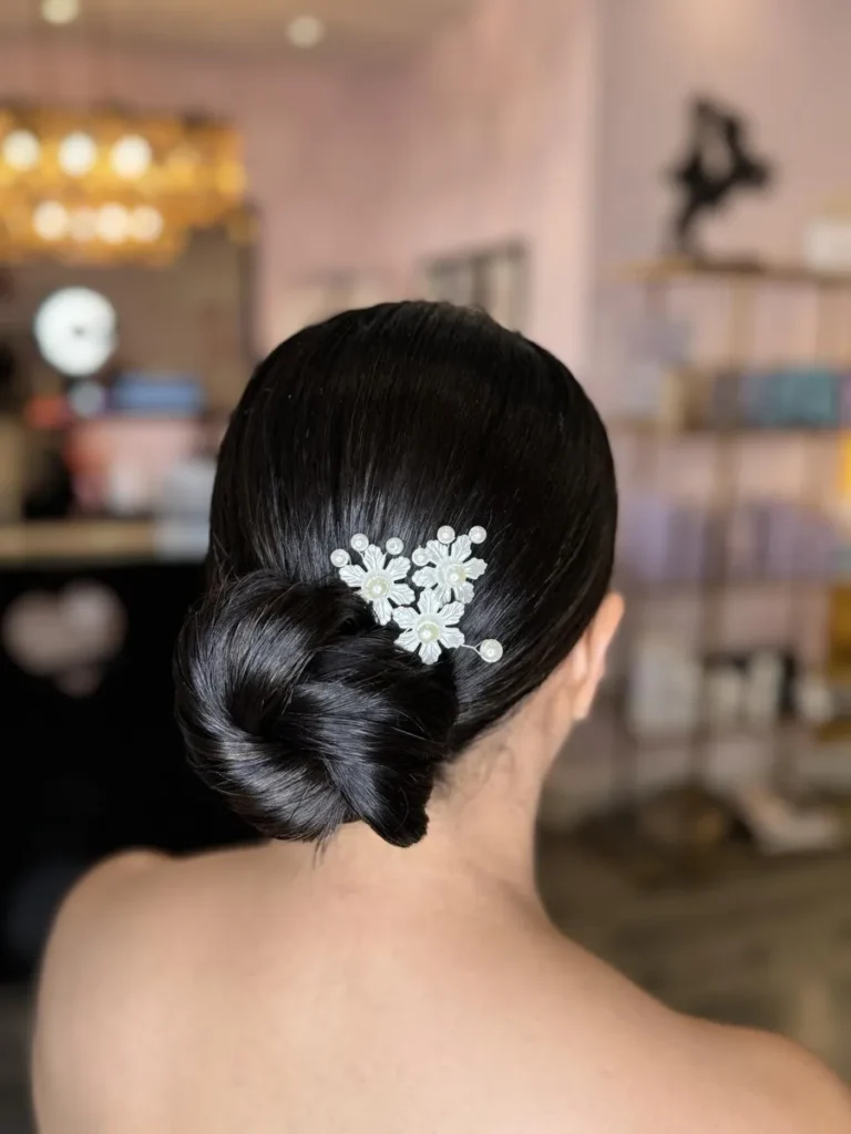 Bridal hairstyle featuring a sleek low bun adorned with delicate pearl flower accessories, perfect for a classic wedding look.