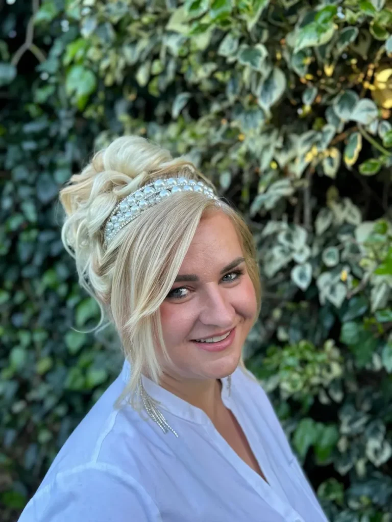 Elegant bridal updo hairstyle featuring a voluminous blonde bun and pearl headband, perfect for wedding day glamour.
