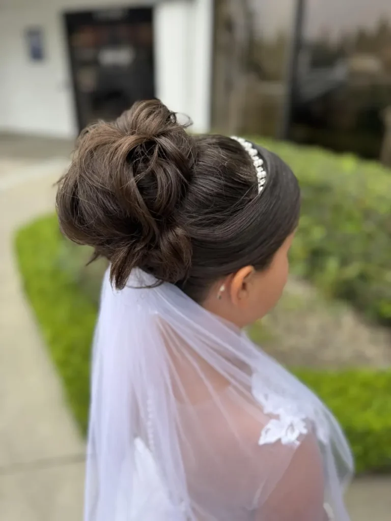 Close up of a bridesmaid's elegant brunette updo hairstyle with a pearl headband and white veil