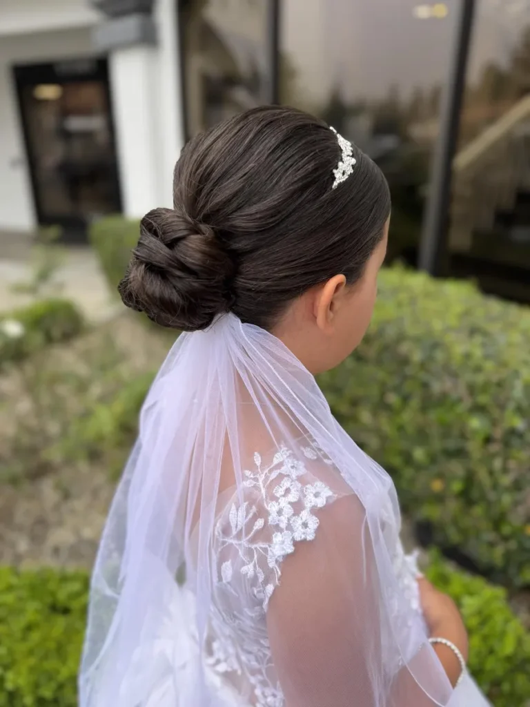 A close up of a bridesmaid with a sleek braided bun and veil featuring floral embroidery.