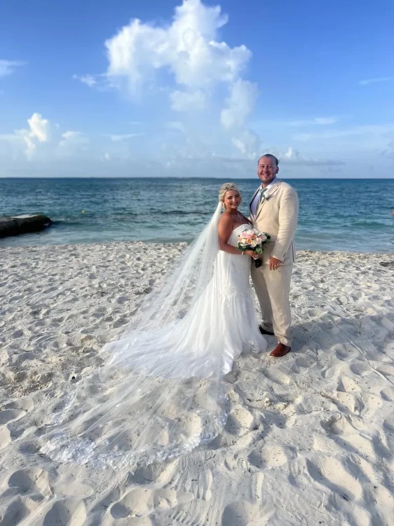 Bride and groom standing on the beach with a long flowing veil on a sunny wedding day