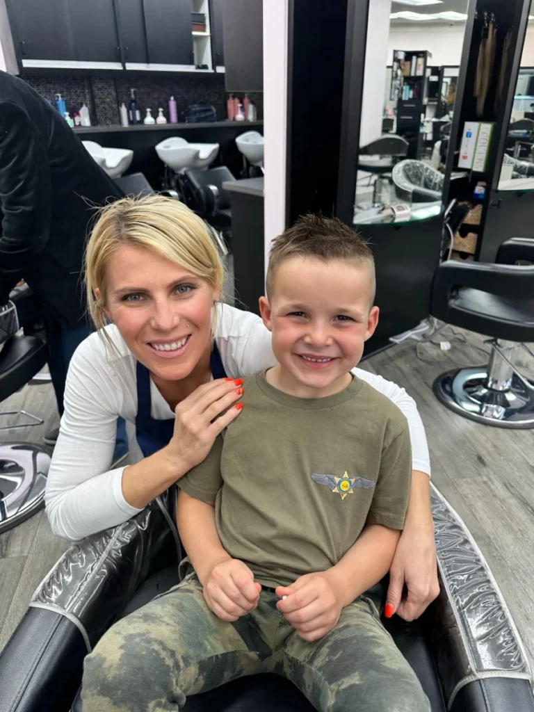 A smiling hairstylist and a young boy after a haircut posing together in the salon chair at Dettycated showcasing a happy client experience.