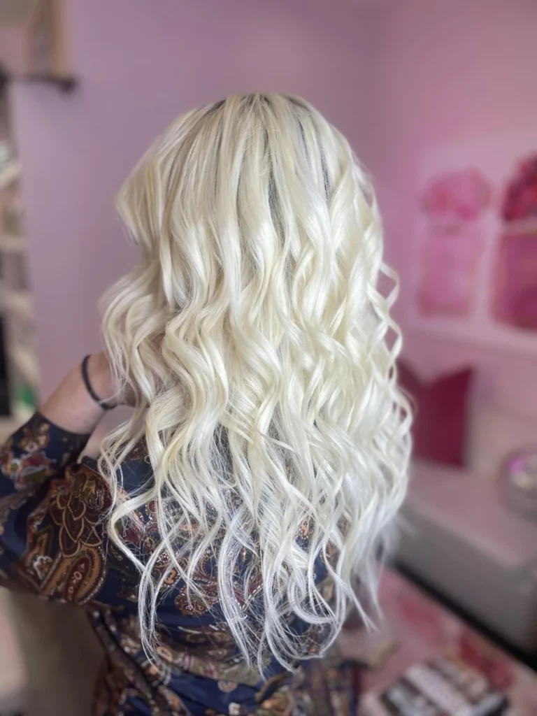 Back view of a client with long platinum blonde hair styled in soft waves captured in a warm salon atmosphere reflecting Dettycated styling precision.